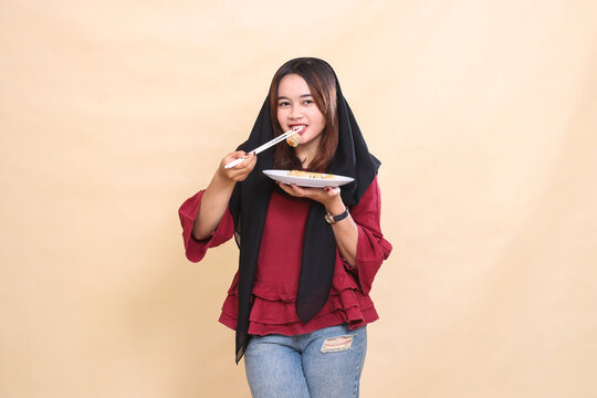 beautiful adult asian woman in red shirt in hijab bites cute dimsum with cheerful chopsticks and carries a plate containing dimsum (chinese food). used for food, health and culinary content