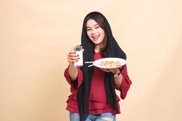 A beautiful elegant Asian woman in a red dress wearing a cheerful hijab holds a glass of milk in front of her and carries a plate containing dimsum (Chinese food). used for food and beverage content