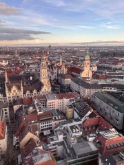 Fototapeta premium A breathtaking aerial view of Munich's cityscape at sunset, showcasing the iconic gothic architecture of the New Town Hall and the St. Peter's Church spires against a backdrop of the distant Alps
