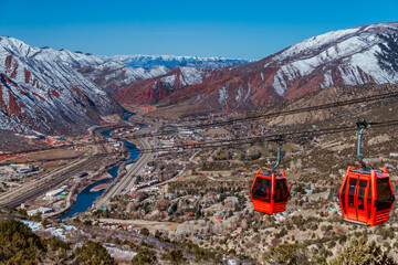 Red Gondola Skilift with red mountains covered with snow in the background and a town down in the valley