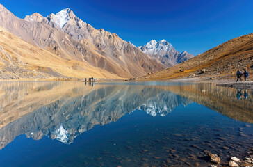 Photo of Himalayan mountains with a blue lake and reflection, people walking along the shore, golden sand dunes