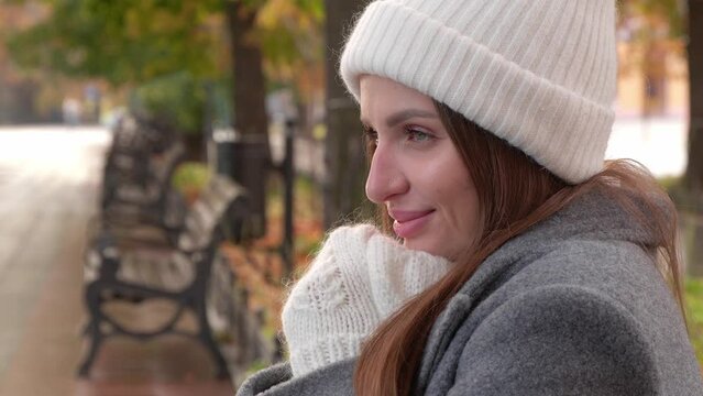 Cute woman in stylish grey coat, warm white hat and mittens in autumn park, closeup