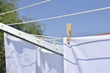 A wooden clothespin holds white laundry on a clothesline outdoors.