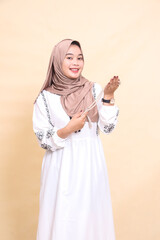 Beautiful young Asian Muslim woman wearing a hijab carrying prayer beads at an angle to the left, smiling elegantly looking at the product promo camera. for advertising, content, banners and Ramadan