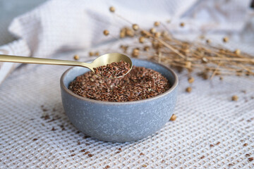 Golden teaspoon of flax seeds in a bowl and dried flax flowers on a cotton napkin background....