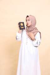 the beauty of a young Asian Muslim woman wearing a hijab kissing and holding the Koran while wearing a prayer beads necklace. for advertising, lifestyle, banners and Ramadan