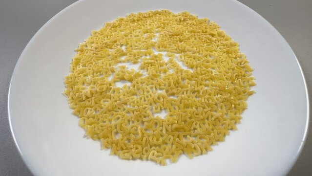 Raw alphabet pasta on dish, close-up in selective focus
