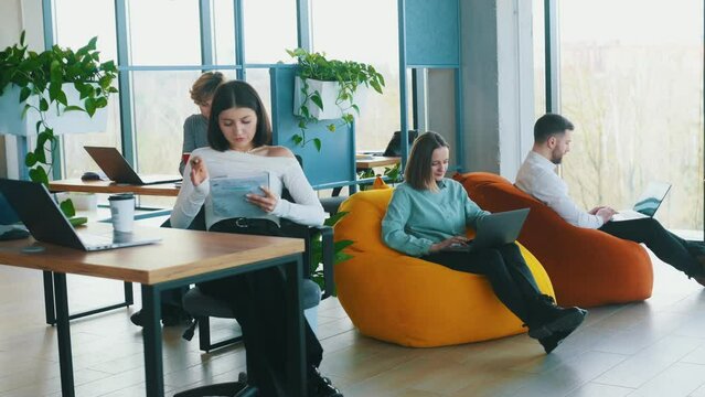 Young woman is sitting and posing. People are working in the office with bean bags chairs in it