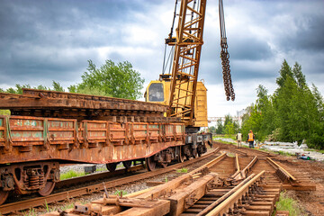A crane is positioned on a train track, conducting maintenance work, with railway ties and tracks visible