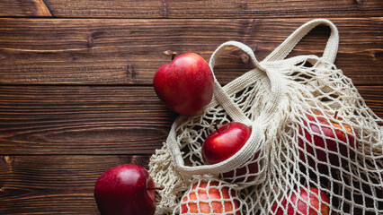 Red apples in a grid bag on a wooden background.