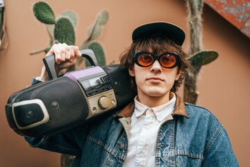 Vintage style young man holding a portable stereo, with cacti in background.