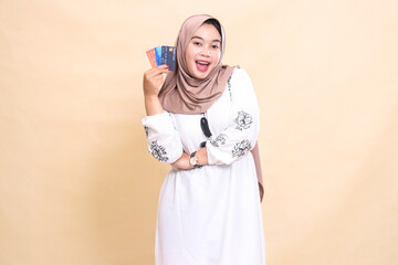 a beautiful Asian Muslim woman wearing a happy hijab with her arms crossed carrying a debit credit card to her side for payment. used for advertising, technology, Eid and Ramadan