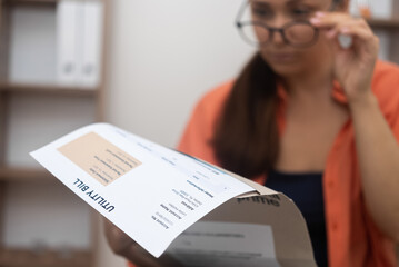 With a furrowed brow, woman pores over utility bills, mentally crunching numbers amidst mounting...