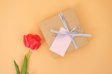Red tulip and gift box with pink note on orange background.