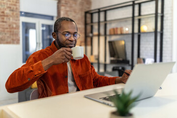 Dark-skinned man in red shirt working at home and having coffee