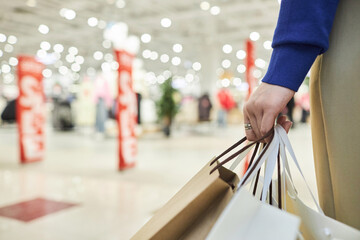 Extreme close up of female hand holding shopping bags standing in mall interior copy space