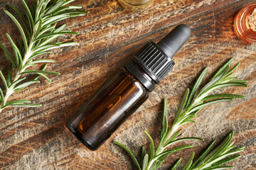 A glass bottle of aromatherapy essential oil with black dropper cap, with fresh rosemary plant