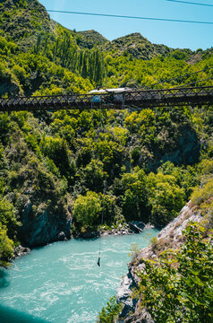 A person is bungee jumping from a river bridge nestled among the mountains. AJ Hackett Kawarau Bungy Centre