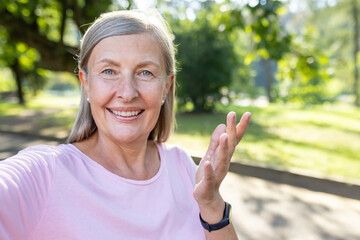Close-up photo of an active senior gray-haired woman walking in the park, talking on the phone with...