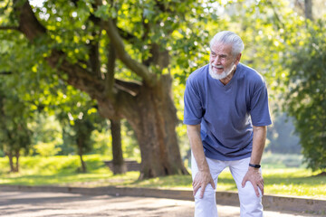 Tired senior gray-haired man is standing bent over in the park and resting after an active walk,...