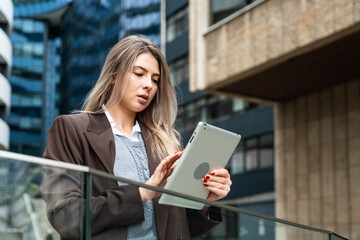 Portrait of a successful business woman using digital tablet in front of modern business office building. Professional female, financial expert, project leader and staff manager standing outdoor
