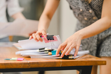 Close-up of hands organizing a stack of documents with colorful binder clips on a wooden table.