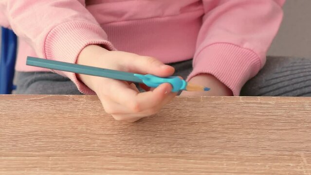The child's hands show the correct grip of the pencil with the help of a convenient silicone pencil attachment in the shape of a dolphin. Teacher training and development of preschoolers.