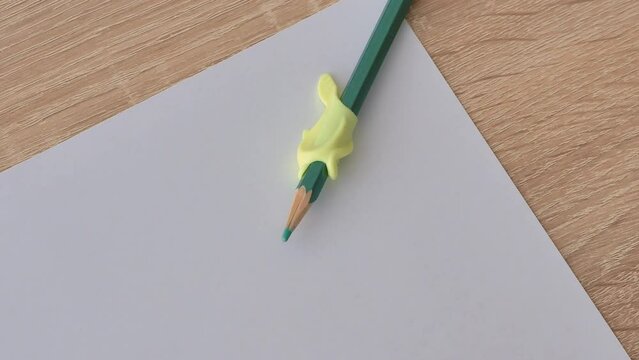 A pencil with a comfortable silicone dolphin attachment lies on a white sheet of paper. We teach the child to hold a pen correctly.