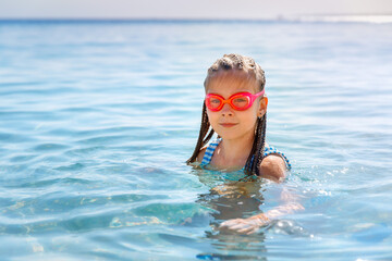  Blonde girl with pink goggles swimming in the sea, looking at the camera, smiling