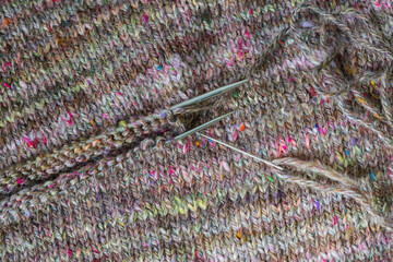 Closeup view of a handmade knitting project with handspun sheep wool, showing two knitting needles...