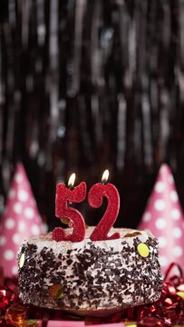 Number fifty-two birthday candle on sweet cake on dark background, 52nd birthday. Blow out the holiday candle.