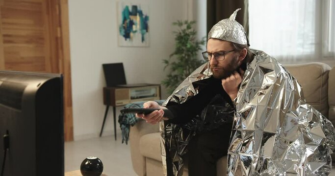A man in a tinfoil hat watches TV.