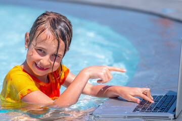 Funny portrait of business child girl working distance on laptop. Pretty young lady typing on computer in the waterpool. Freelance, remote work on vacation.