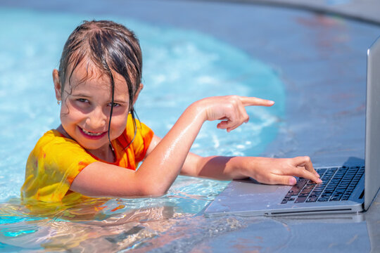 Funny portrait of business child girl working distance on laptop. Pretty young lady typing on computer in the waterpool. Freelance, remote work on vacation. Horizontal image.