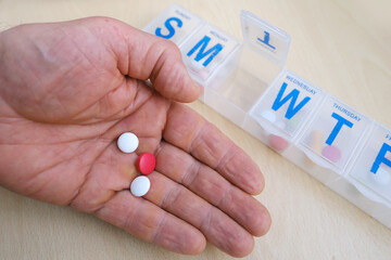 close-up medicinal capsules, pills, vitamins in male palm, plastic pillbox organizer for week, concept controlling regular medication intake, drug dosage, organizing medication intake