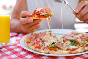 round italian pizza cut into slices on table, male hands take pieces of pizza with salami, cheese,...