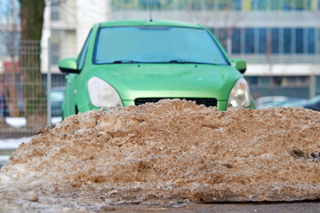 Pile of dirty snow after plowing parking lot. Snowdrift and freezed green car. Сar locked in...