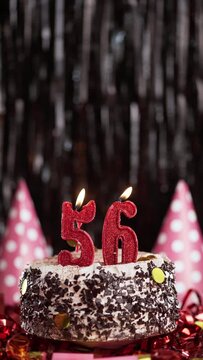Number fifty-six birthday candle on sweet cake on dark background, 56th birthday. Blow out the holiday candle.