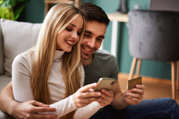Beautiful young happy couple online via smartphone at home