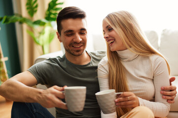 Beautiful young happy couple enjoying coffee at home on sofa - 768742490