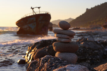 Stacked stones on the beach with sunset and shipwreck in the background at Agios Gordis on corfu