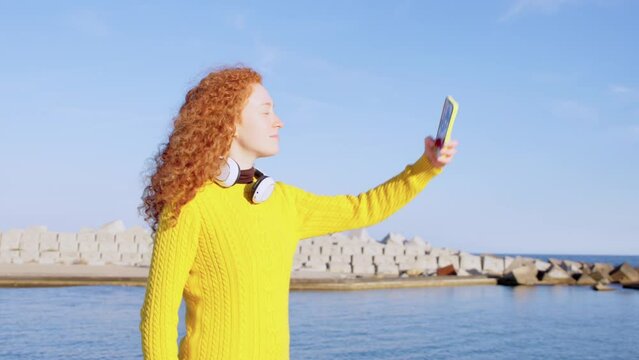 Young redhead woman taking a selfie outdoors at the seaside.