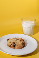 Cookies or biscuits with chocolate chips drops on a white plate. Yellow background. Glass of fresh milk. Great idea for breakfast