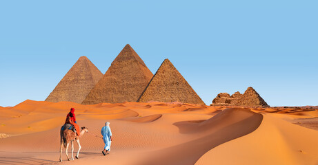 Camels in Giza Pyramid Complex - A woman in a red turban riding a camel across the thin sand dunes - Cairo, Egypt