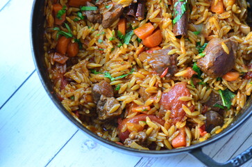 Rice with lamb meat and vegetables on a plate on a wooden table