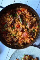 Rice with lamb meat and vegetables on a plate on a wooden table