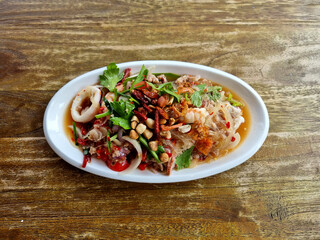 Spicy Glass Noodle Salad with prawn and calamari on wooden table.