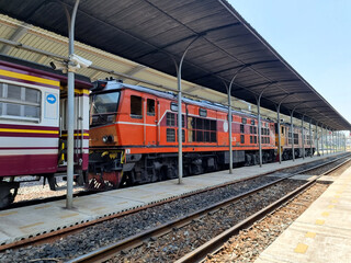 Thai passenger trains are stationary at the railway station platform.