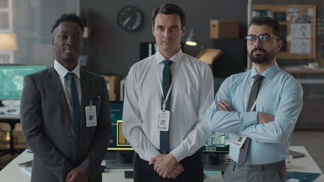 Medium slowmo portrait of ethnically diverse male team of cybersecurity officers posing wearing formalwear and badges posing for camera in office
