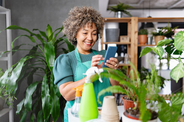 Mature mixed race smiling woman gardener working in home garden, using plant identification app for mobile phone - 768776036
